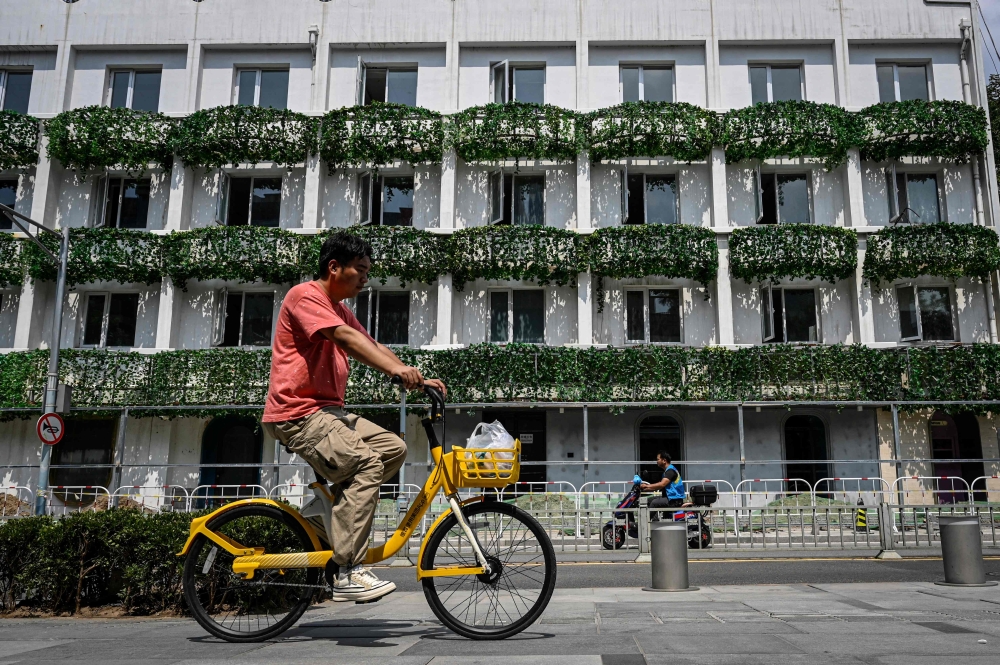 A man rides a bicycle past a building under renovation at a shopping mall in Beijing on August 15, 2023. (Photo by Jade Gao / AFP)