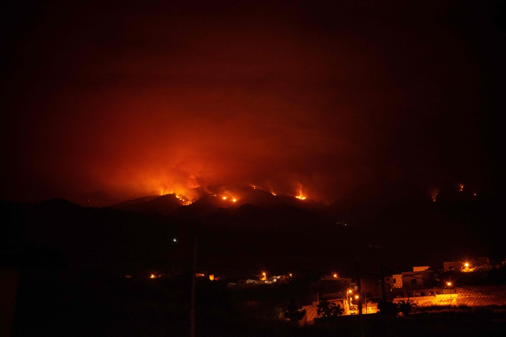 A picture taken in the night of August 19, 2023 shows the fronts of the forest fire on hills above houses, in the Guimar valley on the Canary Island of Tenerife. Photo by DESIREE MARTIN / AFP