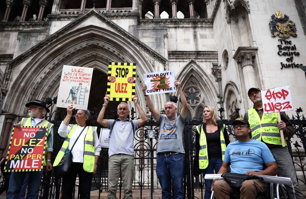 Demonstrators hold placards as they protest against the expansion of the Ultra Low Emission Zone (ULEZ) in London, outside the Royal Courts of Justice, Britain's High Court, in central London on July 28, 2023. Photo by Henry Nicholls / AFP
