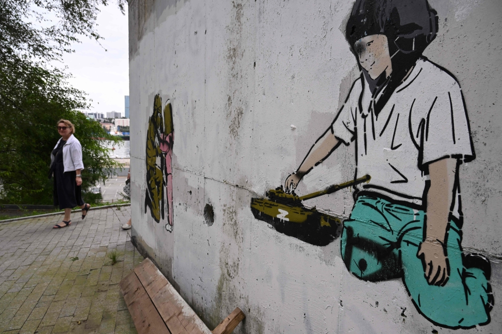 A woman walks behind a mural showing a child playing with a tank bearing the Z letter, a tactical insignia of Russian troops in Ukraine, in the Russian port city of Vladivostok on September 13, 2023. (Photo by Natalia Kolesnikova / AFP)