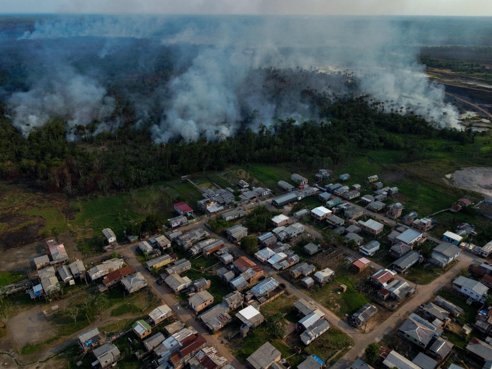 The smoke from a fire in a forest area approaches houses at the Cacau Pirera District in Iranduba, Amazonas state, Brazil on September 25, 2023. (Photo by Michael Dantas / AFP)