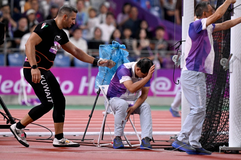 An official reacts in pain after his leg was injured by a stray hammer thrown by Ali Zankawi (L) who attempts to stem the bleeding. (Photo by William West / AFP)