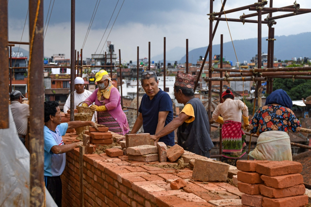 In this photograph taken on June 22, 2023, heritage conservationist and Kathmandu Valley Preservation Trust director Rohit Ranjitkar (4R) speaks with labourers at a reconstruction site in the Patan Durbar Square of Lalitpur district on the outskirts of Kathmandu. Photo by Prakash MATHEMA / AFP