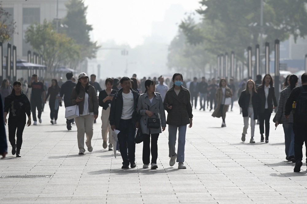People walk along a business street in Beijing on October 31, 2023. (Photo by WANG Zhao / AFP)