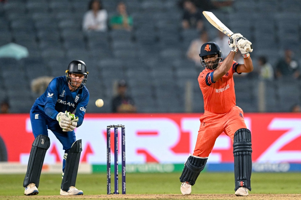 Netherlands' Teja Nidamanuru plays a shot as England's captain Jos Buttler (L) watches during the 2023 ICC Men's Cricket World Cup one-day international (ODI) match between England and Netherlands at the Maharashtra Cricket Association Stadium in Pune on November 8, 2023. (Photo by Punit PARANJPE / AFP)