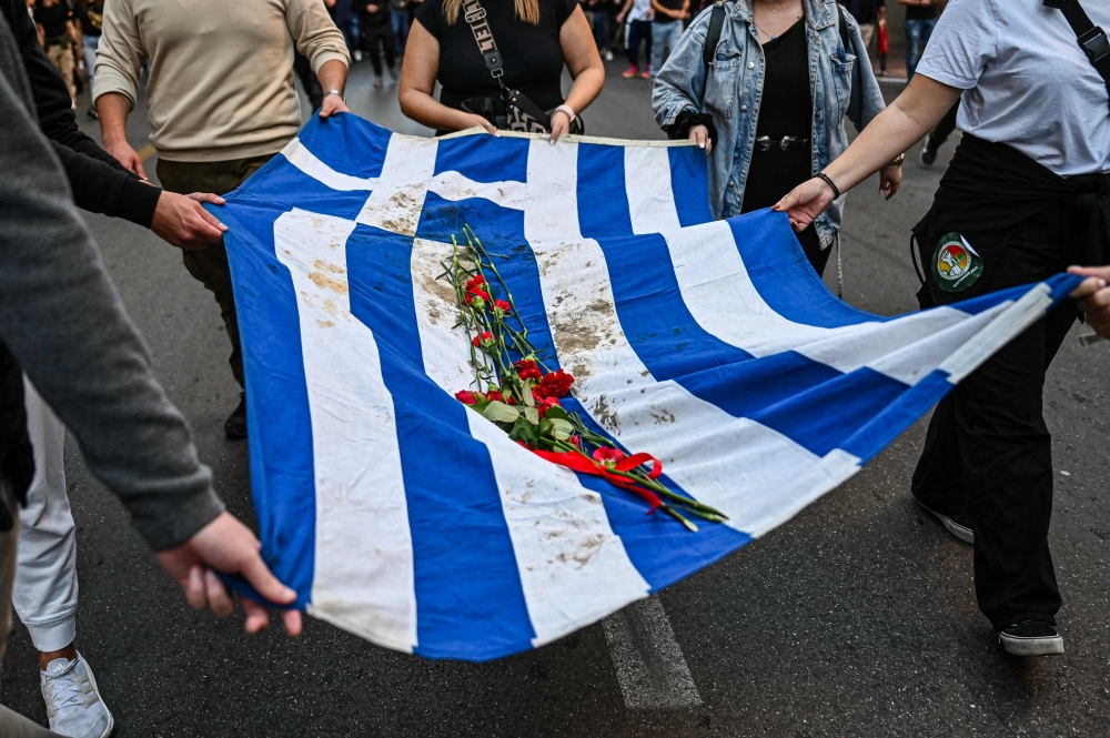 Demonstrators and students symbolically carry a blood-stained Greek flag with red flowers, during a march towards the US embassy in Athens on November 17, 2023, to commemorate the 50th anniversary of the 1973 students' uprising against a US-backed junta. (Photo by Theophile Bloudanis / AFP)
