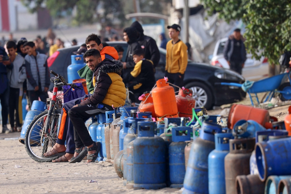 People sit with empty canisters waiting for them to be filled with cooking gas from a tank that entered the Palestinian enclave via the Rafah crossing with Egypt on November 25, 2023. (Photo by SAID KHATIB / AFP)