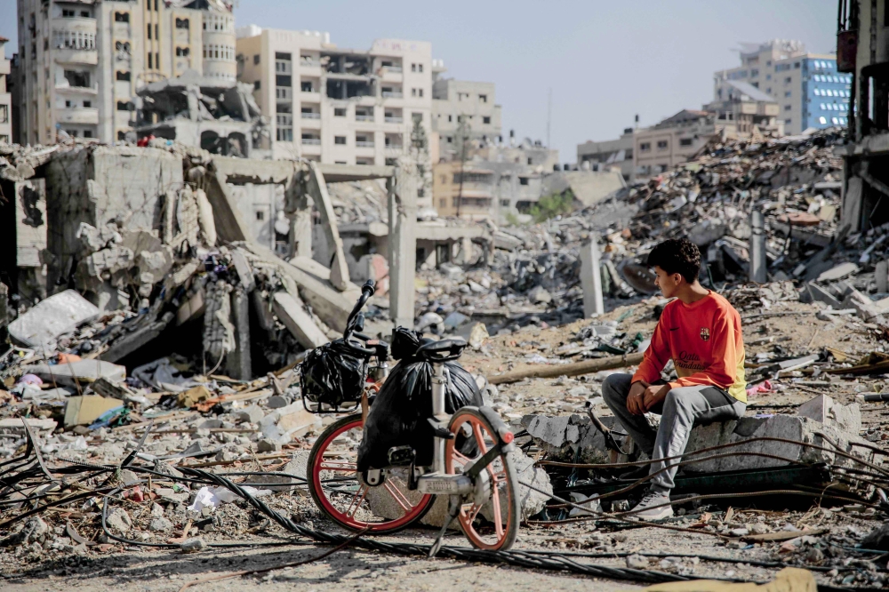 A Palestinian youth sits next to his bicycle amid the rubble of destroyed buildings in Gaza City on the northern Gaza Strip following weeks of Israeli bombardment, as a four-day ceasefire took effect on November 24, 2023. Photo by AFP
