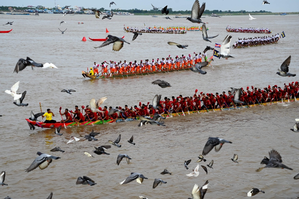 Pigeons fly past as participants row dragon boats during a competition as part of the Water Festival on the Tonle Sap river in Phnom Penh on November 26, 2023. (Photo by Tang Chhin Sothy / AFP)