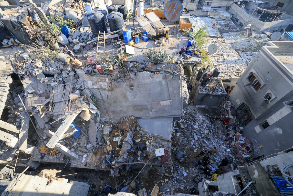 People inspect the damage amid the rubble of a building destroyed during Israeli bombardment overnight in Rafah on the southern Gaza Strip on December 7, 2023. Photo by MAHMUD HAMS / AFP