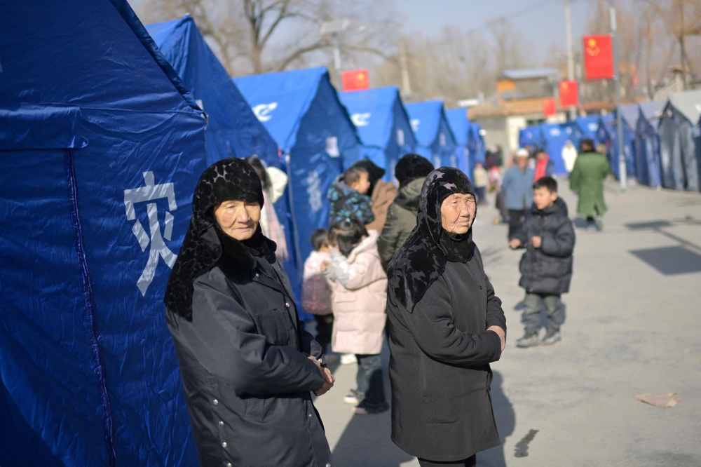 Earthquake-affected residents look on beside aid tents erected in a school compound at Gaoli village in Jishishan County in northwest China's Gansu province on December 20, 2023. (Photo by Pedro Pardo / AFP)
 