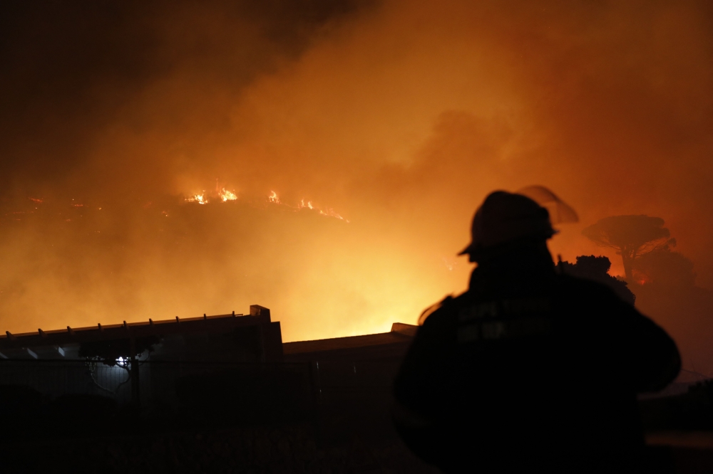 A South African firefighter is seen near a house surounded by flames as a fire rages on the mountain above Simon's Town on December 20, 2023. (Photo by GIANLUIGI GUERCIA / AFP)