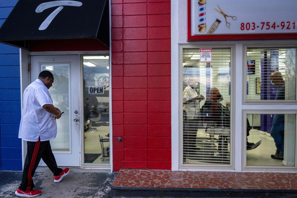 Co-owner Chris Toliver (L) arrives as his father Herbert Toliver (C) trims hair and talks with customers at Toliver's Mane Event Barber Shop in Charleston, South Carolina, on February 2, 2024. (Photo by Jim WATSON / AFP)
