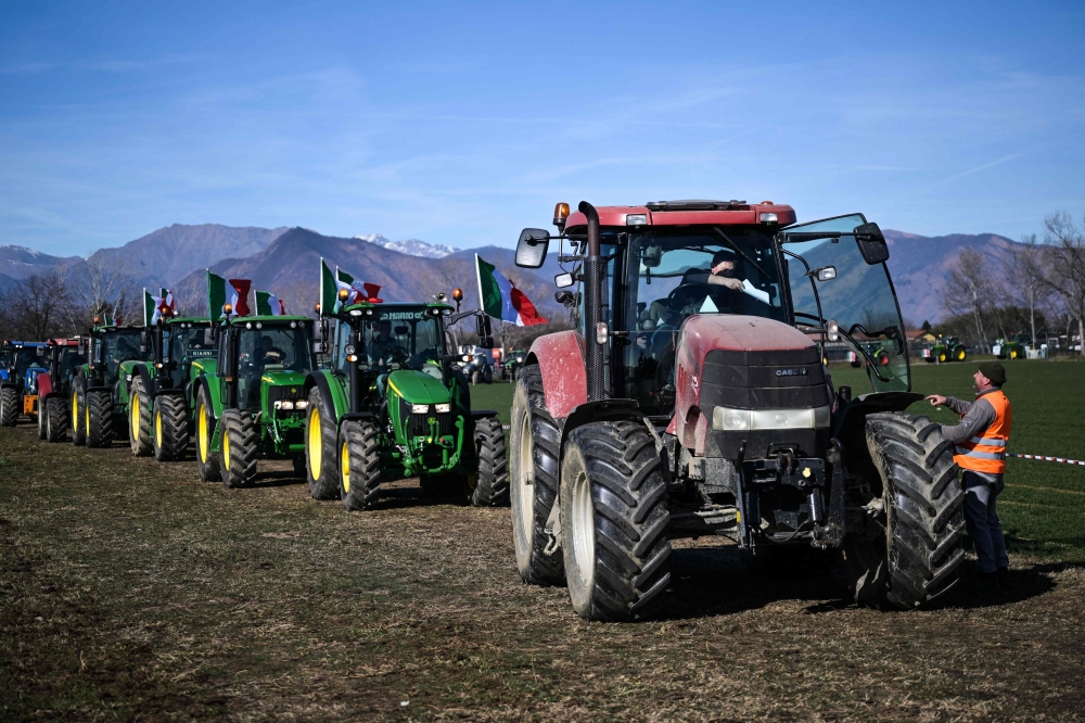 Farmers drive tractors in a field alongside the road during a demonstration near the highway in Rivoli, near Turin, on February 5, 2024. (Photo by MARCO BERTORELLO / AFP)
