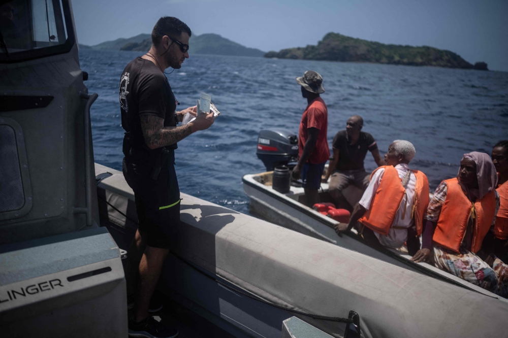 A policeman of the French Air and Border Police (PAF) inspects a villager's boat documentation during a patrol to intercept boats sailing clandestinely from the Comoros to the French Indian Ocean island of Mayotte, on February 17, 2024. (Photo by JULIEN DE ROSA / AFP)
