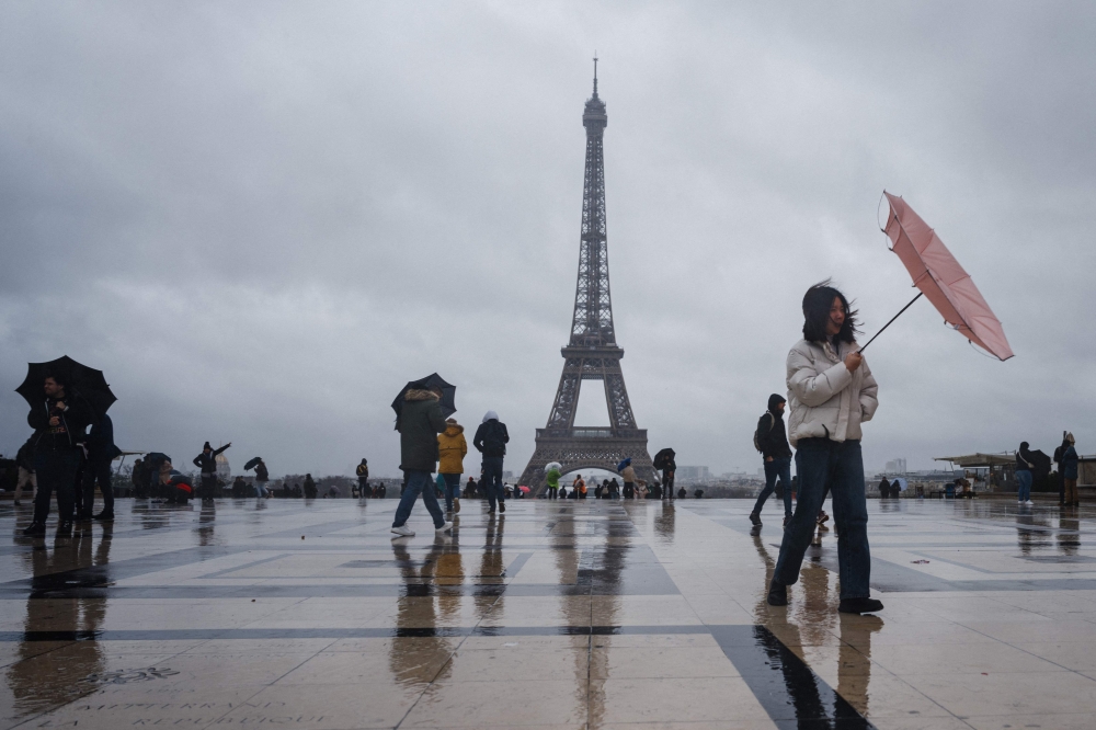 A tourist tries to protect herself with an umbrella on a rainy day at the Esplanade du Trocadero with the Eiffel Tower in the background, which is closed to the public on the fourth day of its staff's strike, in Paris on February 22, 2024. Photo by Dimitar DILKOFF / AFP