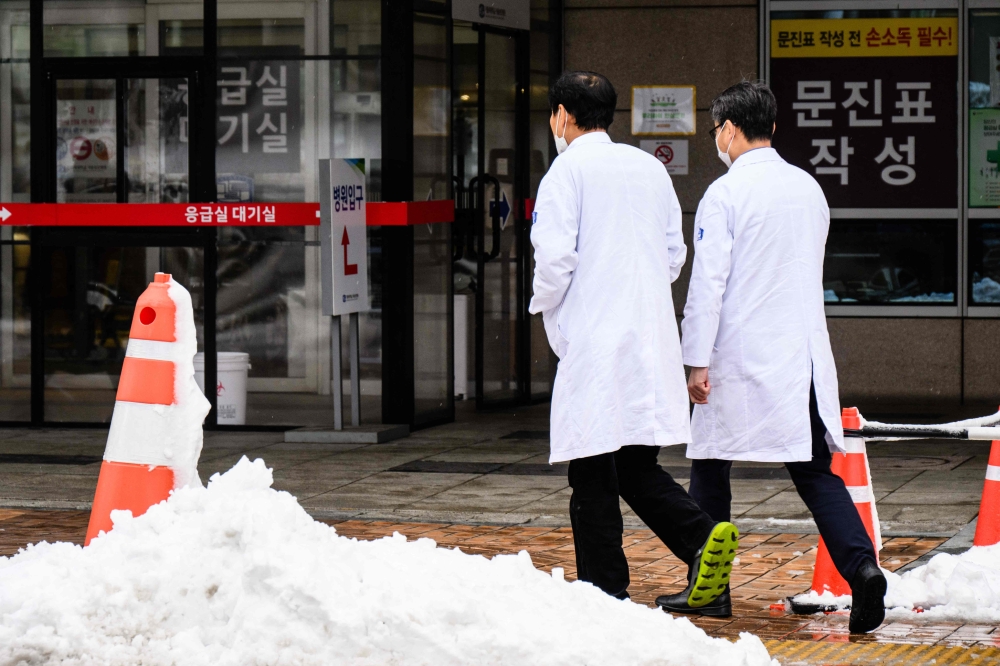 Medical workers walk outside a hospital after snowfall in Seoul on February 22, 2024. (Photo by Anthony Wallace / AFP)