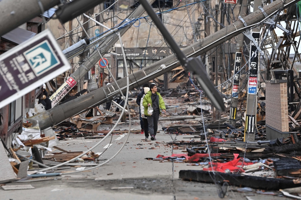 People walk past fallen utility poles and damaged buildings in the city of Wajima, Ishikawa prefecture on January 4, 2024, after a major 7.5 magnitude earthquake struck the Noto region in Ishikawa prefecture on New Year's Day. Photo by Kazuhiro NOGI / AFP

