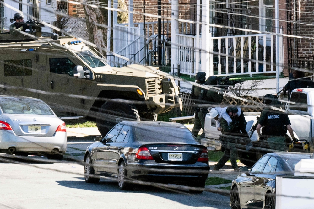 Police evacuate a person (L bottom) from a home in Trenton New Jersey, on March 16, 2024, after reports of a gunman, who is suspected of a shooting spree in Pennsylvania, was barricaded in the house. (Photo by Joe LAMBERTI / AFP)
