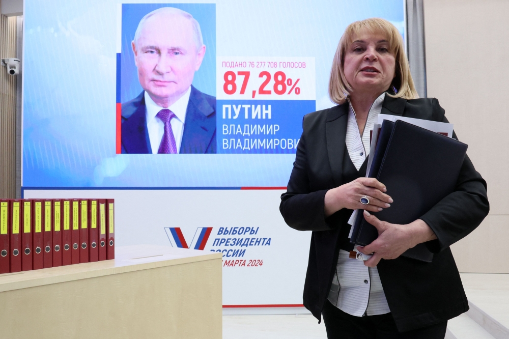 Russia's Central Electoral Commission (CEC) head Ella Pamfilova walks past a screen displaying a portrait of re-elected Russian President Vladimir Putin following the announcement of the official results in the three-day presidential election in Moscow on March 21, 2024. (Photo by Stringer / AFP)