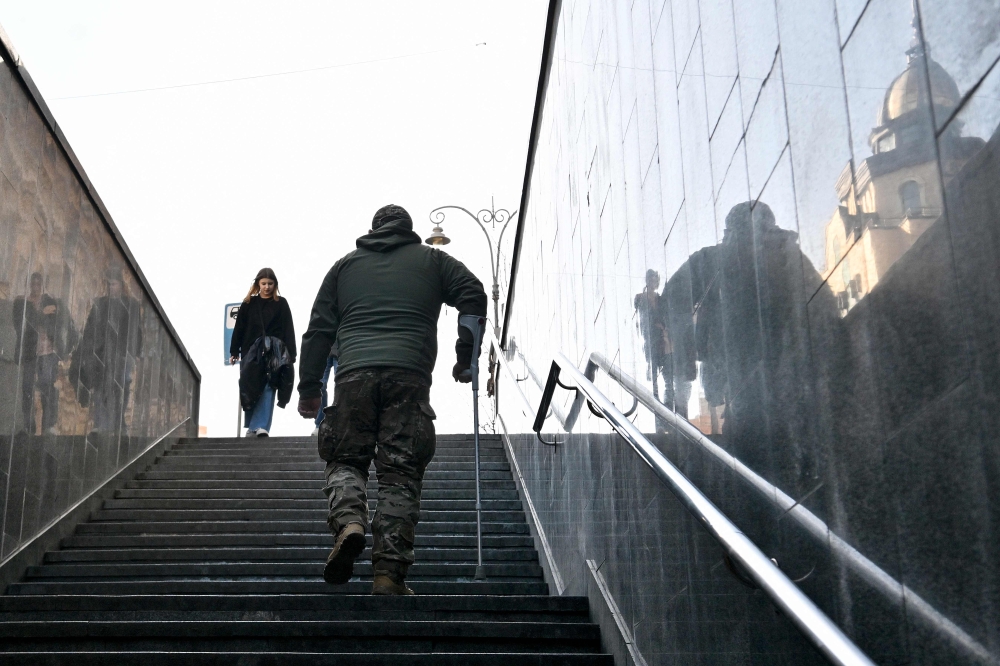 A wounded Ukrainian serviceman climbs stairs from an underground pedestrian way in the center of Kyiv on March 27, 2024, amid Russian invasion in Ukraine. Photo by Sergei SUPINSKY / AFP.