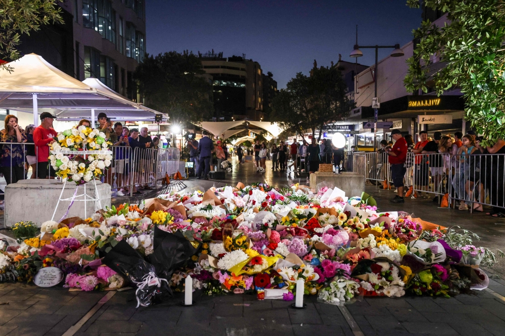 Members of the public look at flowers placed outside the Westfield Bondi Junction shopping mall in Sydney on April 14, 2024, the day after a 40-year-old knifeman with mental illness roamed the packed shopping centre killing six people and seriously wounding a dozen others. (Photo by DAVID GRAY / AFP)