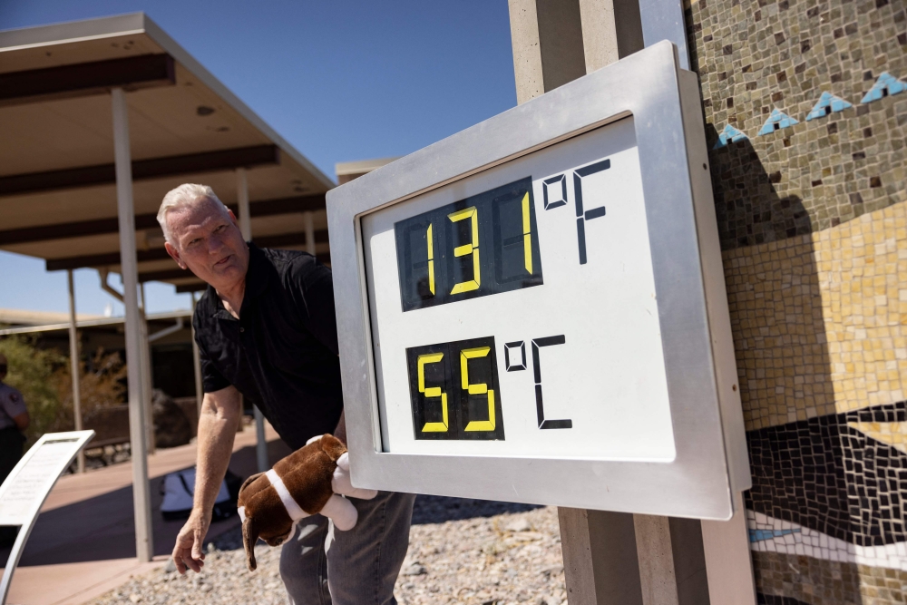 A visitor reacts as he poses next to a thermometer reading “131F, 55C” at the Visitor Center in Death Valley National Park, near Furnace Creek, during a heatwave on July 7, 2024. (Photo by Etienne Laurent / AFP)