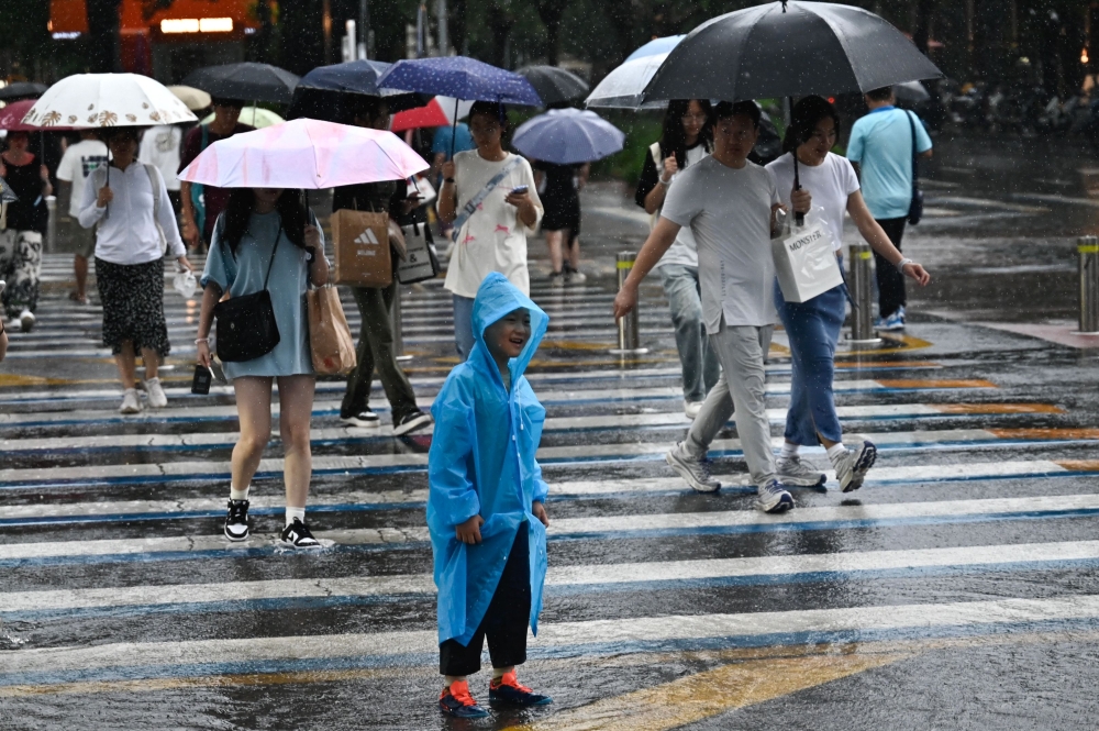 People walk through a rainstorm in Beijing on July 30, 2024. (Photo by Pedro PARDO / AFP)