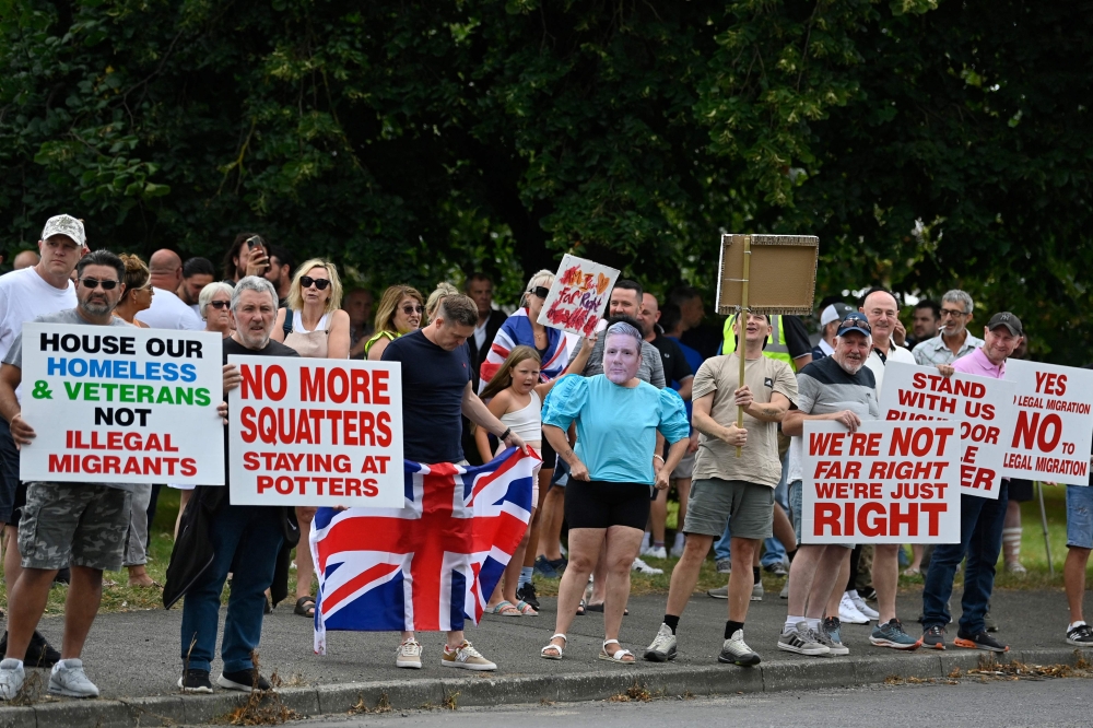 Protesters, including one wearing a mask of Britain's Prime Minister Keir Starmer, hold placards during a 'Enough is Enough' demonstration called by far-right activists near a hotel housing asylum seekers in Aldershot on August 4, 2024.  (Photo by Justin Tallis / AFP)