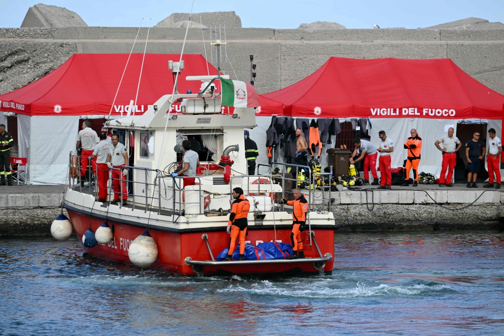 Divers of the Vigili del Fuoco, the Italian Corps. of Firefighters arrive in Porticello harbor near Palermo, with a third body at the back of the boat on August 21, 2024, two days after the British-flagged luxury yacht Bayesian sank. (Photo by Alberto PIZZOLI / AFP)
