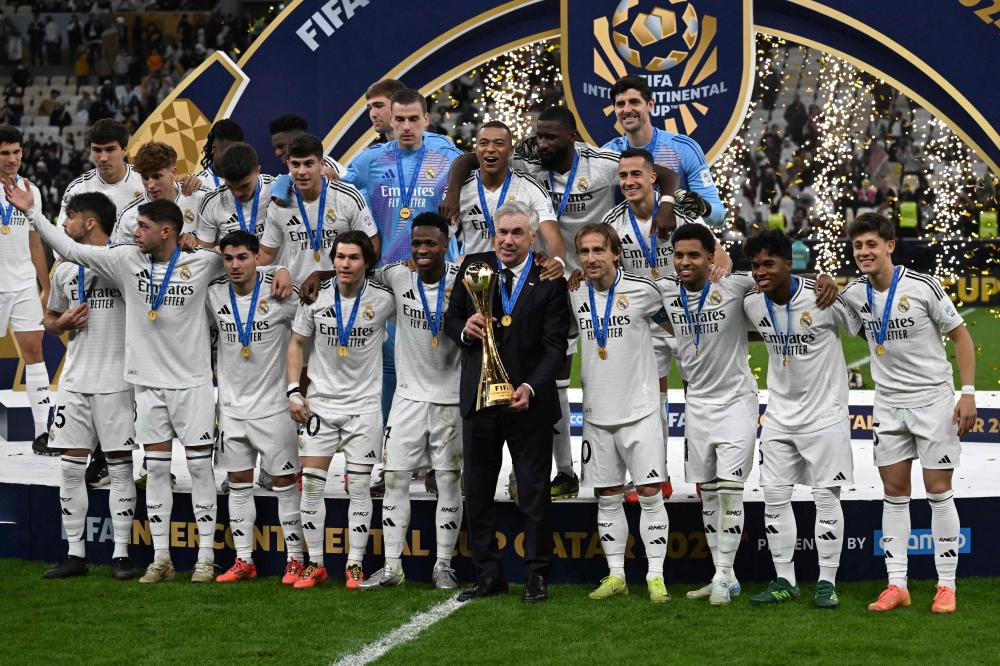 Real Madrid's Italian coach Carlo Ancelotti holds the tournament trophy as he poses with his players for the group picture at the podium ceremony after the 2024 FIFA Intercontinental Cup final football match between Spain's Real Madrid and Mexico's Pachuca at the Lusail Stadium in Doha on December 18, 2024. (Photo by Mahmud Hams / AFP)

