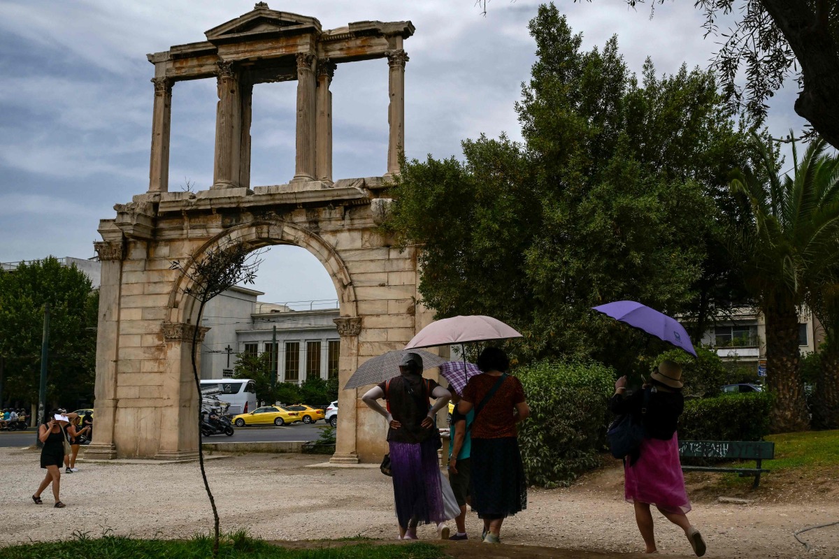 (FILES) Tourists holding umbrellas walk in front of the ancient Roman Andrian Gate, during a hot day in Athens on June 13, 2024. (Photo by Aris MESSINIS / AFP)

