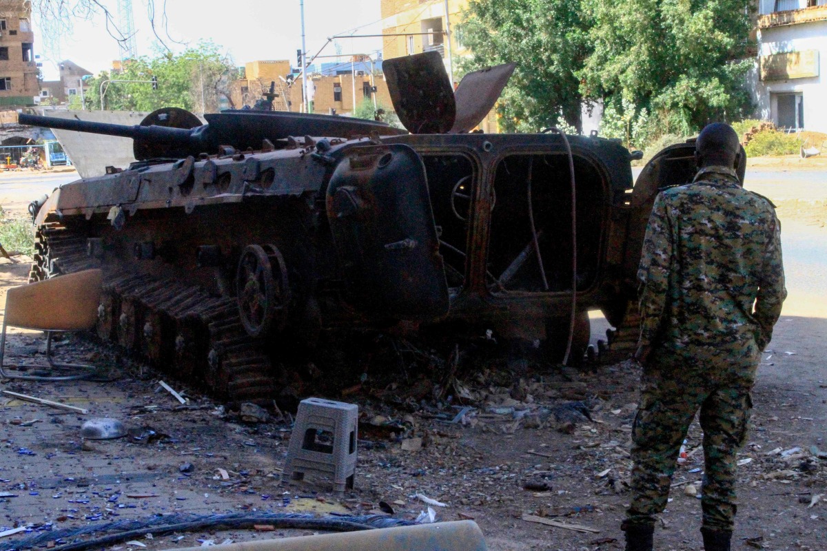 This picture shows a fighter in front of a burnt military vehicle, in Khartoum North, on March 17, 2025. Nearly two years of war between the army and the paramilitary Rapid Support Forces (RSF) have left large swathes of Sudan's capital unrecognisable. (Photo by Ebrahim Hamid / AFP)

