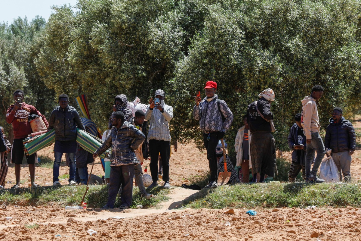 People leave with their belongings from a makeshift camp for migrants from sub-Saharan Africa as authorities dismantle the camp at al-Amra on the outskirts of the Tunisian city of Sfax on April 24, 2025. (Photo by Mohamed KHALIL / AFP)

