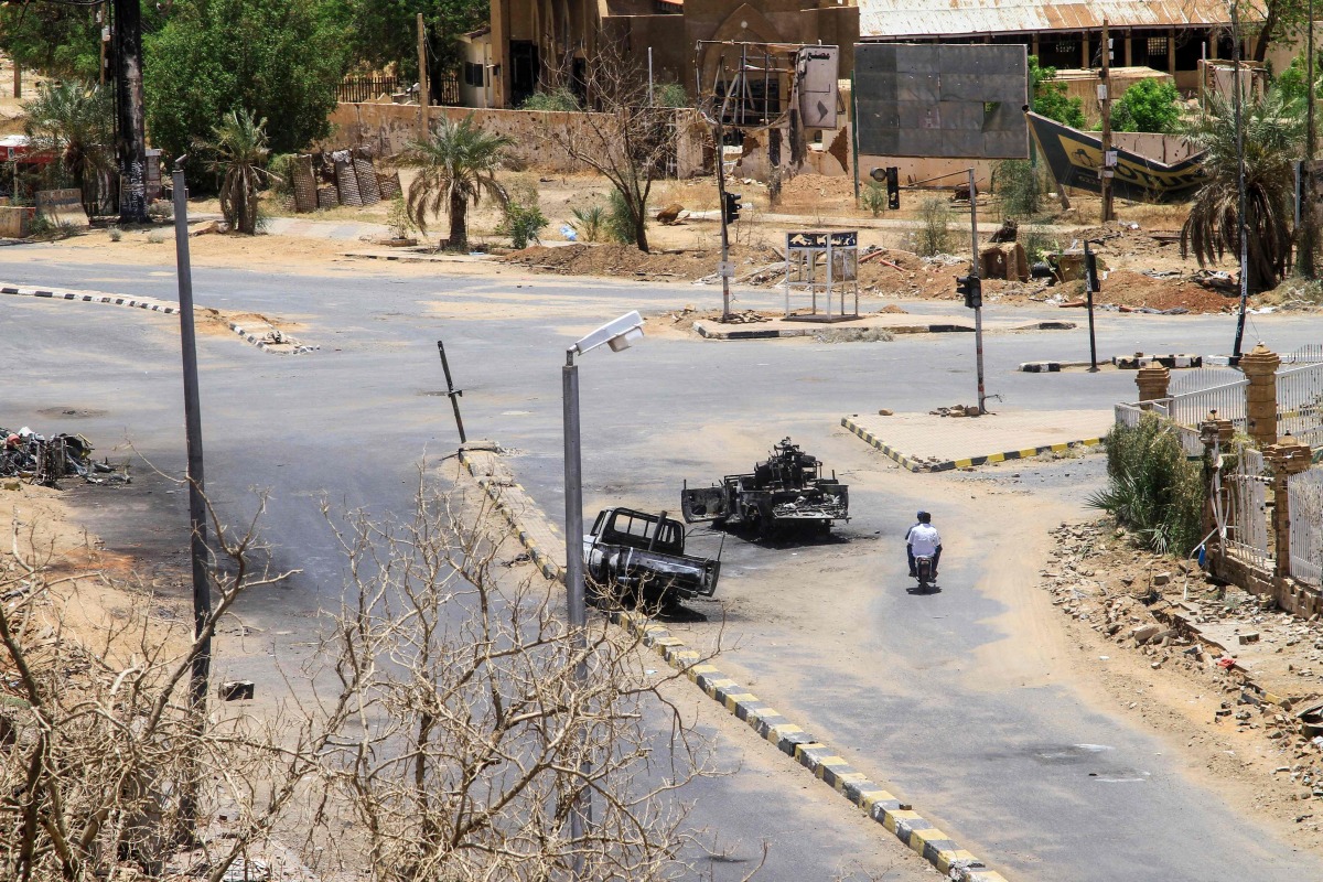 Sudanese men ride on a motorcycle past destroyed military vehicles in front of a hospital in Khartoum on April 28, 2025. (Photo by AFP)
