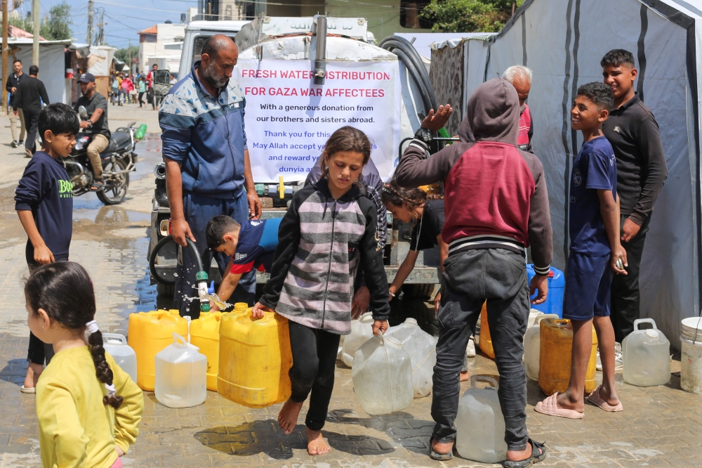A Palestinian girl ferries water containers back from a distribution point at the Nuseirat refugee camp in the central Gaza Strip on May 5, 2025. (Photo by Eyad BABA / AFP)