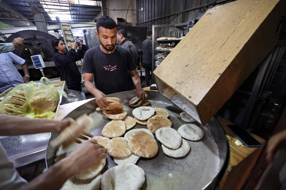 Employees of a bakery in Deir el-Balah in the central Gaza Strip, fill bags with freshly-baked bread, after Israel allowed limited humanitarian aid to enter the Palestinian territory on May 22, 2025. (Photo by Eyad Baba / AFP)
