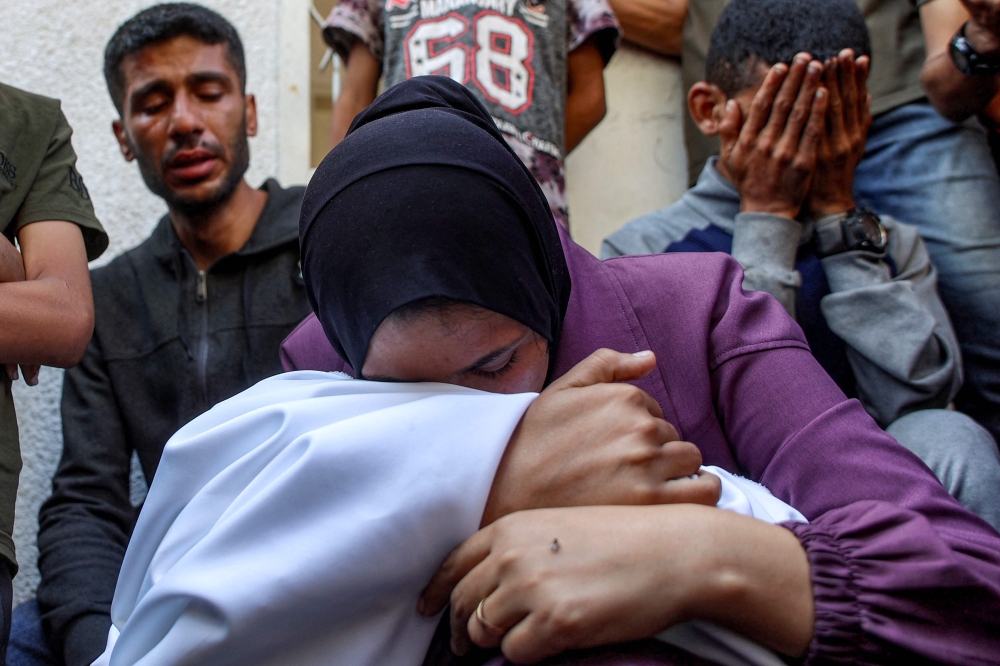 A woman mourns over the body of a victim who was killed during overnight Israeli bombardment as she sits at al-Shifa hospital in Gaza City on June 4, 2025. (Photo by Omar Al-Qattaa / AFP)