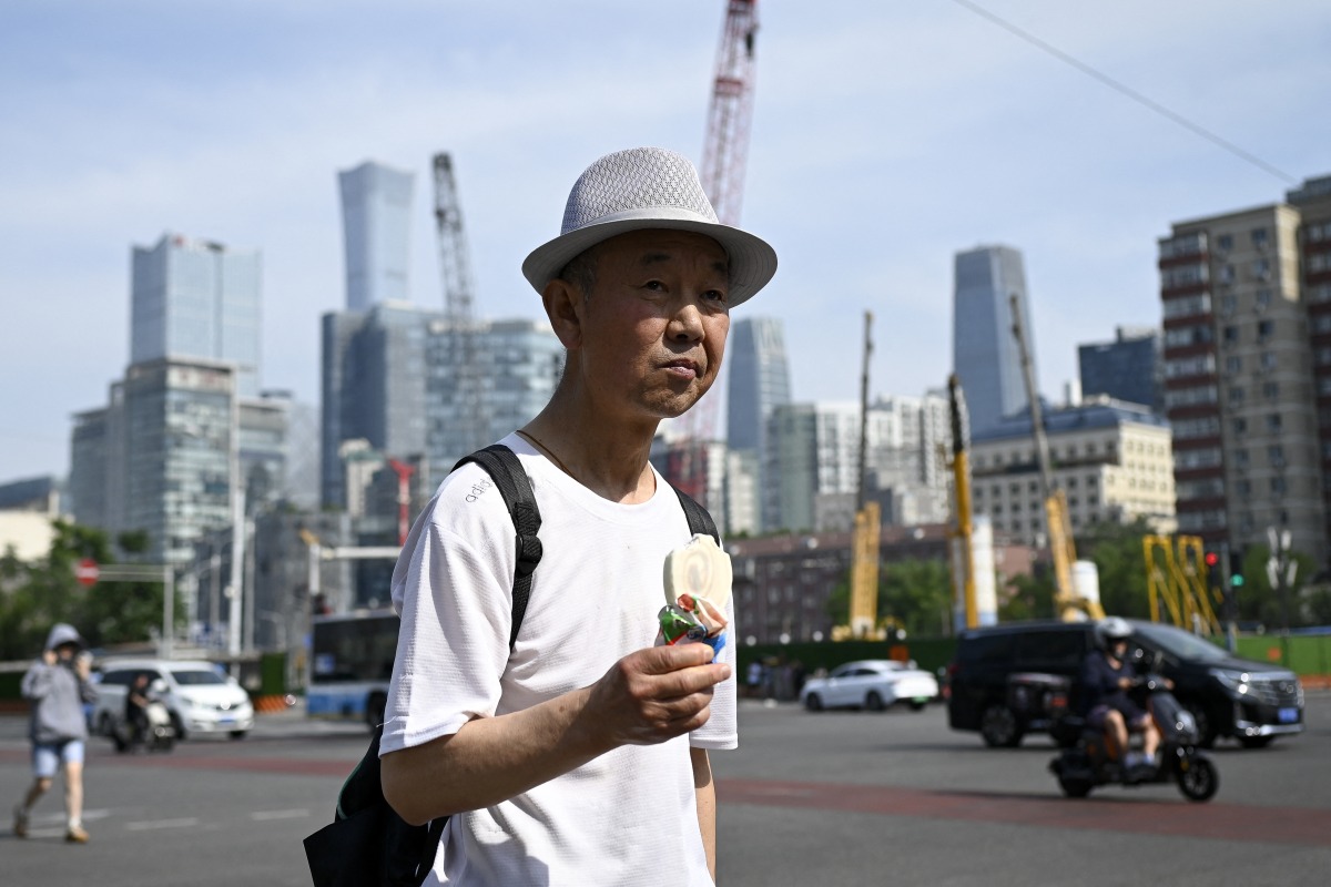 A man holding an ice cream crosses a street in Beijing on June 23, 2025. Photo by WANG Zhao / AFP.
