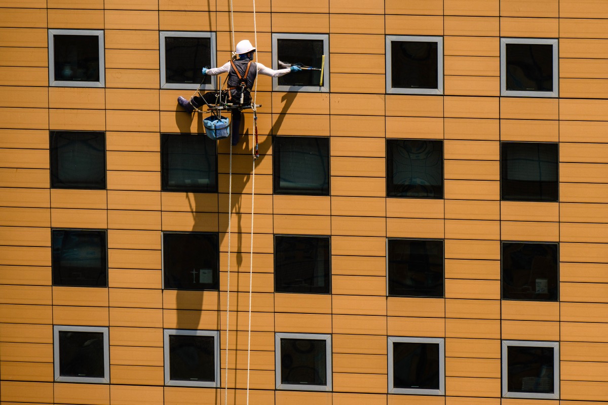 Photo used for representational purposes. A window cleaner uses a squeegee while rappelling down a commercial building in Seoul on June 23, 2025. (Photo by Anthony WALLACE / AFP)