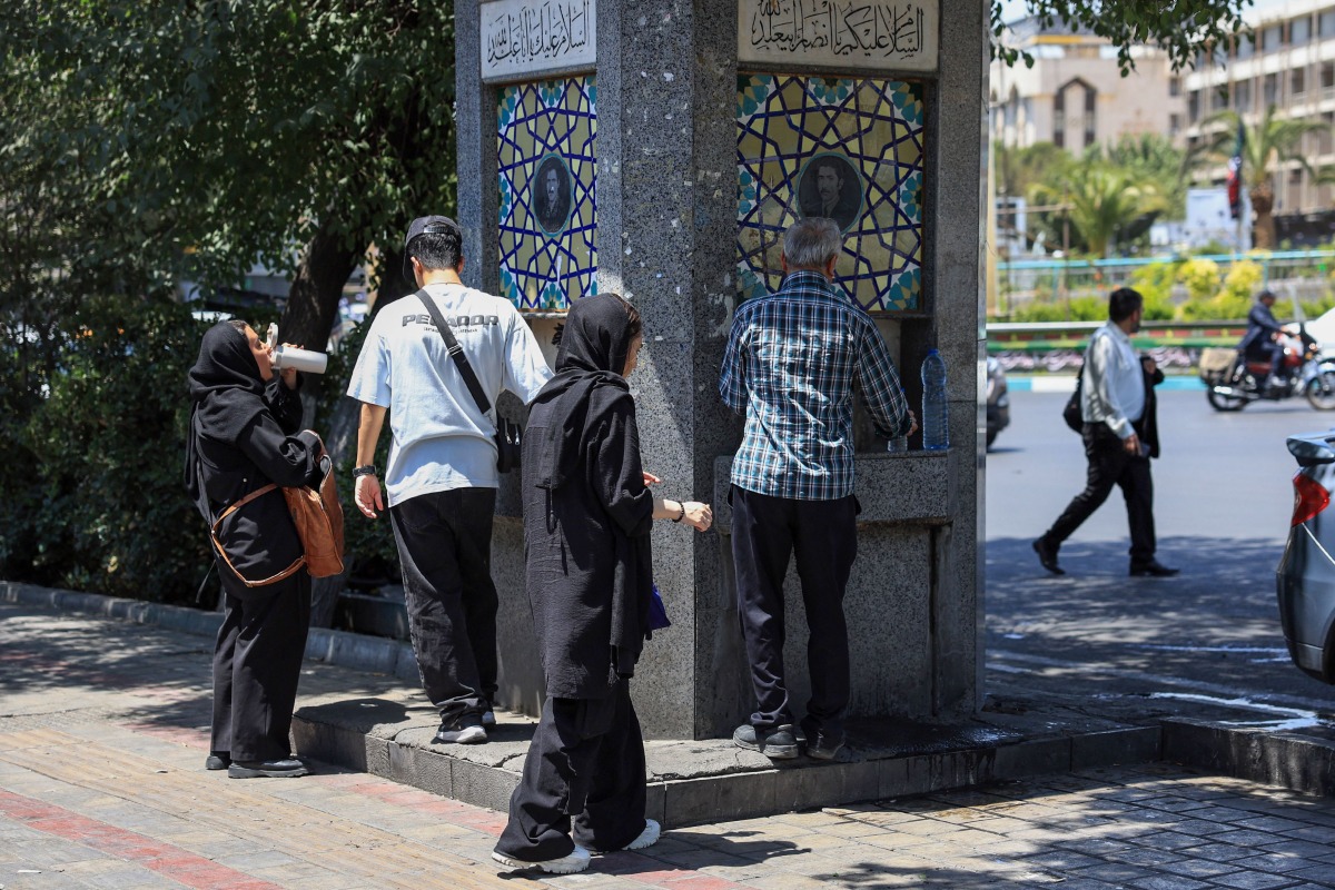 Iranians drink water from a public street fountain amid soaring temperatures in Tehran on July 22, 2025. (Photo by AFP)
