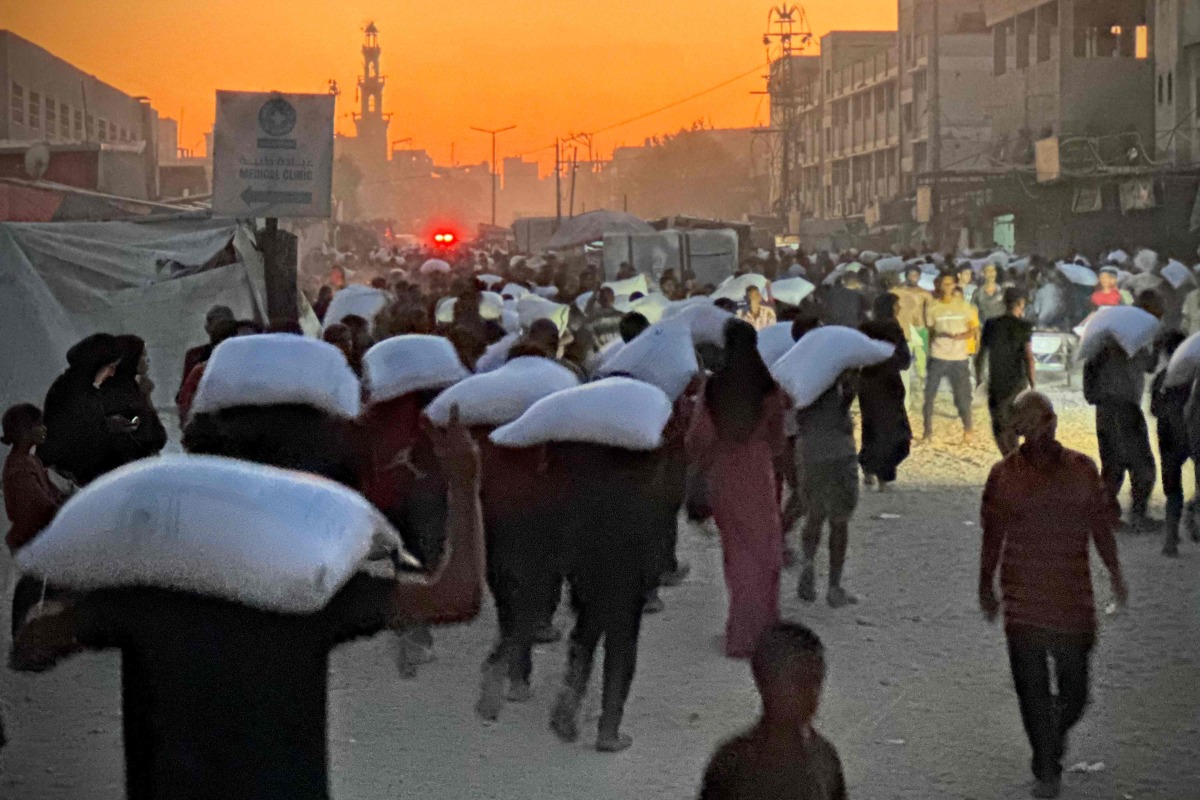 Men walk carrying sacks of flour that were taken from a raided truck carry sacks of flour after raiding a truck that was carrying foodstuffs, in Khan Yunis in the southern Gaza Strip on July 22, 2025. (Photo by AFP)