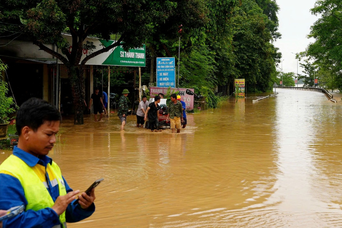 A worker uses his phone on a flooded street in Vietnam's north-central Nghe An province on July 23, 2025, following heavy rains brought by Tropical Storm Wipha. (Photo by AFP)