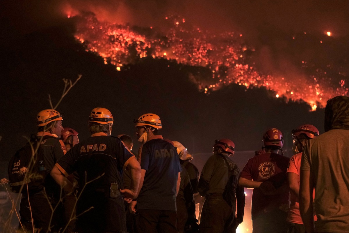 Firefighters attempt to extinguish a wildfire as smoke and flames rise from a forested area in the Gursu district of Bursa early on July 27, 2025. (Photo by ONUR YURTSEVER / AFP)