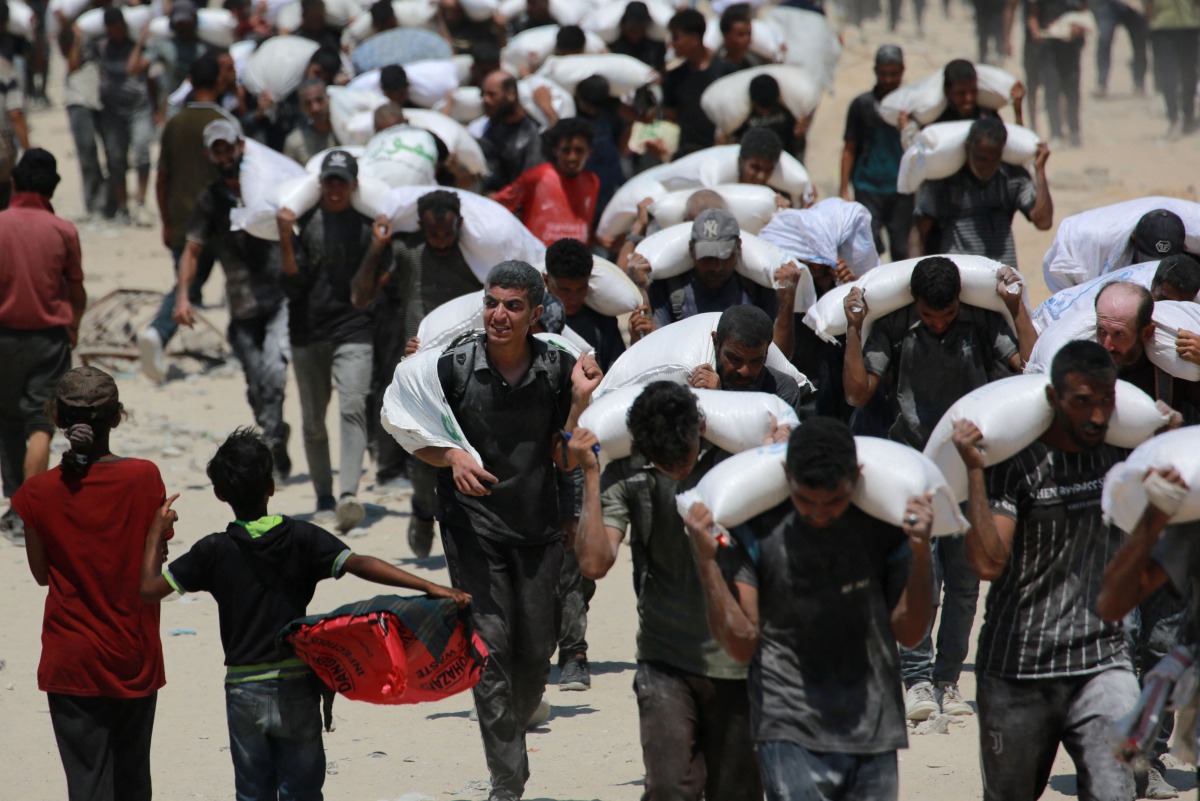 Palestinian walk carrying sacks of flour near Jabalia, in the northern Gaza Strip, on July 27, 2025, after planes dropped aid into Gaza. Photo by BASHAR TALEB / AFP