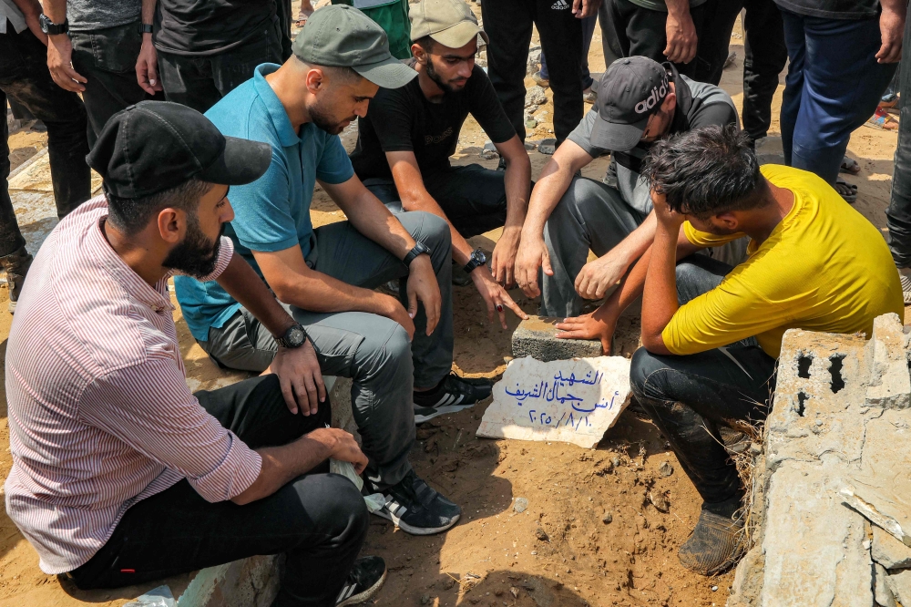 Mourners sit around the grave of Al Jazeera correspondent Anas al-Sharif, who was killed alongside other journalists in an overnight Israeli strike on their tent in Gaza City, following his burial at the Sheikh Radwan cemetery in Gaza City on August 11, 2025. (Photo by Omar Al-Qattaa / AFP)