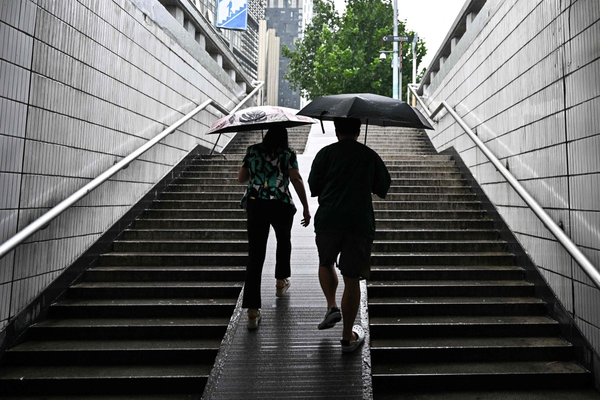 People use umbrellas to protect themselves from the rain in Beijing on August 27, 2025. (Photo by Pedro PARDO / AFP)