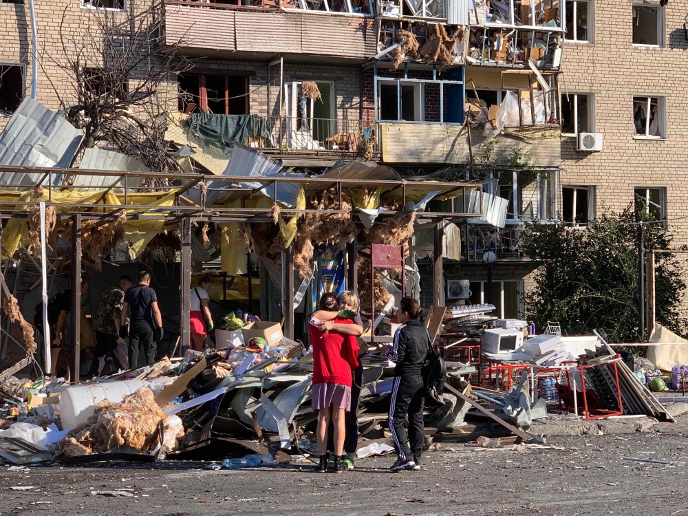 Local residents embrace each other next to a damaged residential building following an air attack in Zaporizhzhia on August 30, 2025. (Photo by Marina Moiseyenko / AFP)