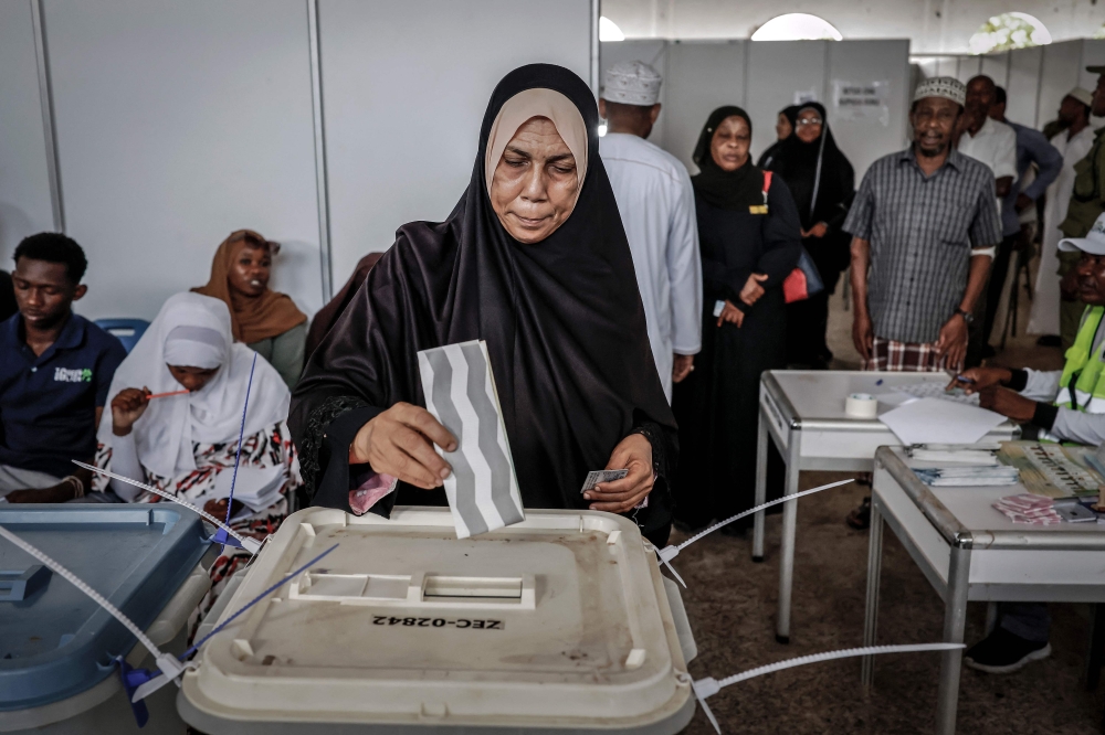 A voter casts her ballot while others queue at the Maundi voting centre in Stone Town on October 29, 2025, during Tanzania's presidential elections. Photo by Marco Longari / AFP