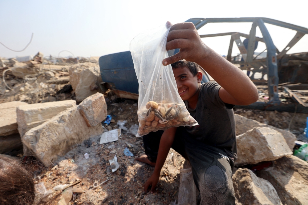 A Palestinian boy shows a bag of seeds and nuts he collected from the sand along the verge of a road near in the Nuseirat refugee camp in the central Gaza Strip, on November 9, 2025. (Photo by Eyad Baba / AFP)